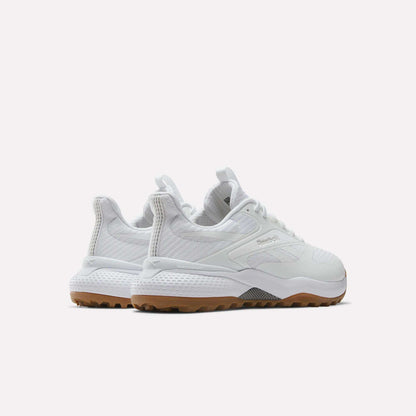 A pair of Reebok Nano Golf Shoes in white with textured details and tan rubber soles, made from lightweight FlexWeave, shown from a rear three-quarter angle on a plain white background.