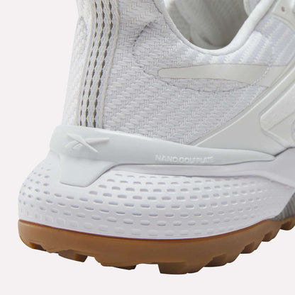 Close-up of the heel of a white Reebok Nano Golf Shoe with textured patterns, tan rubber outsole, and embossed Reebok logo. "NANO COLPLATE" above the midsole highlights its lightweight FlexWeave construction.