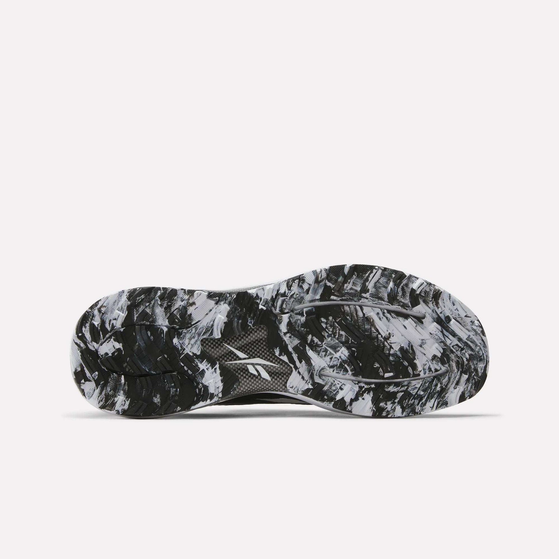 The image displays the black and white marbled sole of Reebok Nano Golf Shoes, viewed from below to showcase the grip pattern and tread design that complement performance foam for enhanced comfort.