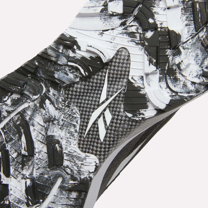 Close-up of the Reebok Nano Golf Shoes sole, showing a textured black and white pattern with a central Reebok logo. Rugged, angular tread shapes enhance traction, while performance foam offers comfort on the course.