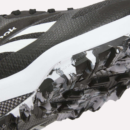 Close-up of Reebok Nano Golf Shoes in black and white, highlighting the textured sole with rugged tread pattern and FlexWeave upper for enhanced durability, plus a visible white logo.