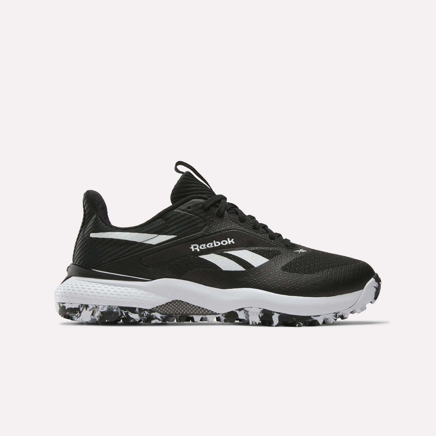 The Reebok Nano Golf Shoes feature a black FlexWeave upper, white detailing and logo, a white midsole, and a black-and-white speckled outsole, displayed on a plain light background.