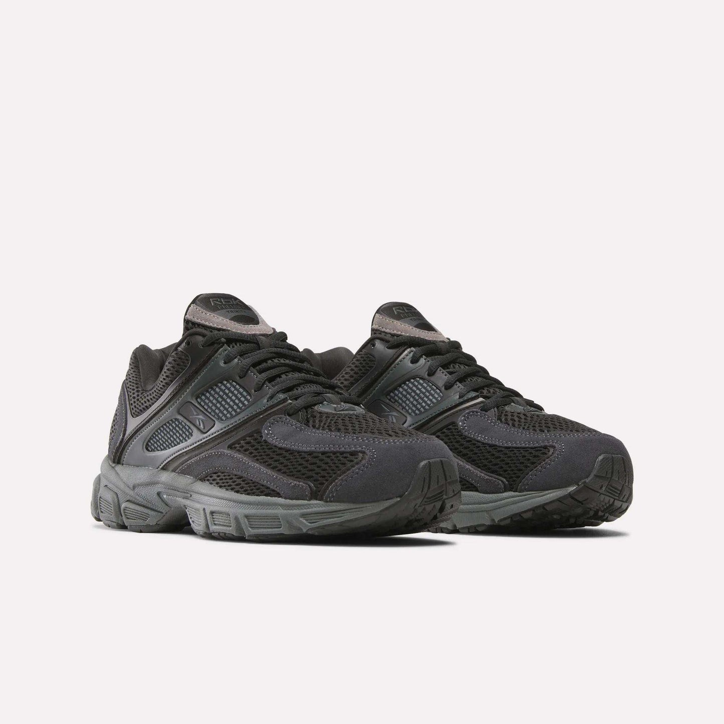 A pair of Reebok Premier Trinity Shoes for women in black, featuring mesh and synthetic overlays, thick rubber soles, and lace-up closures, shown on a plain white background for a retro running vibe.