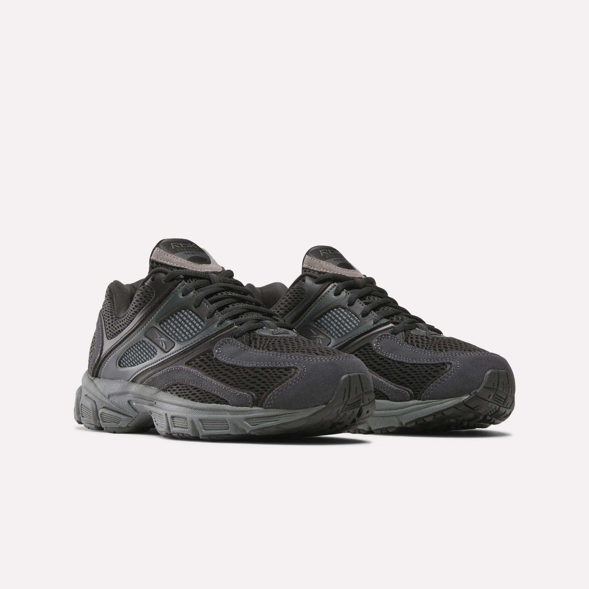 A pair of Reebok Premier Trinity Shoes for women in black, featuring mesh and synthetic overlays, thick rubber soles, and lace-up closures, shown on a plain white background for a retro running vibe.