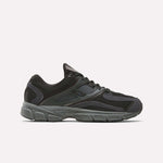 The Reebok Premier Trinity Shoes are black and dark gray athletic sneakers inspired by retro running, with mesh and synthetic overlays, a thick cushioned sole, and lace-up design, shown on a plain white background.
