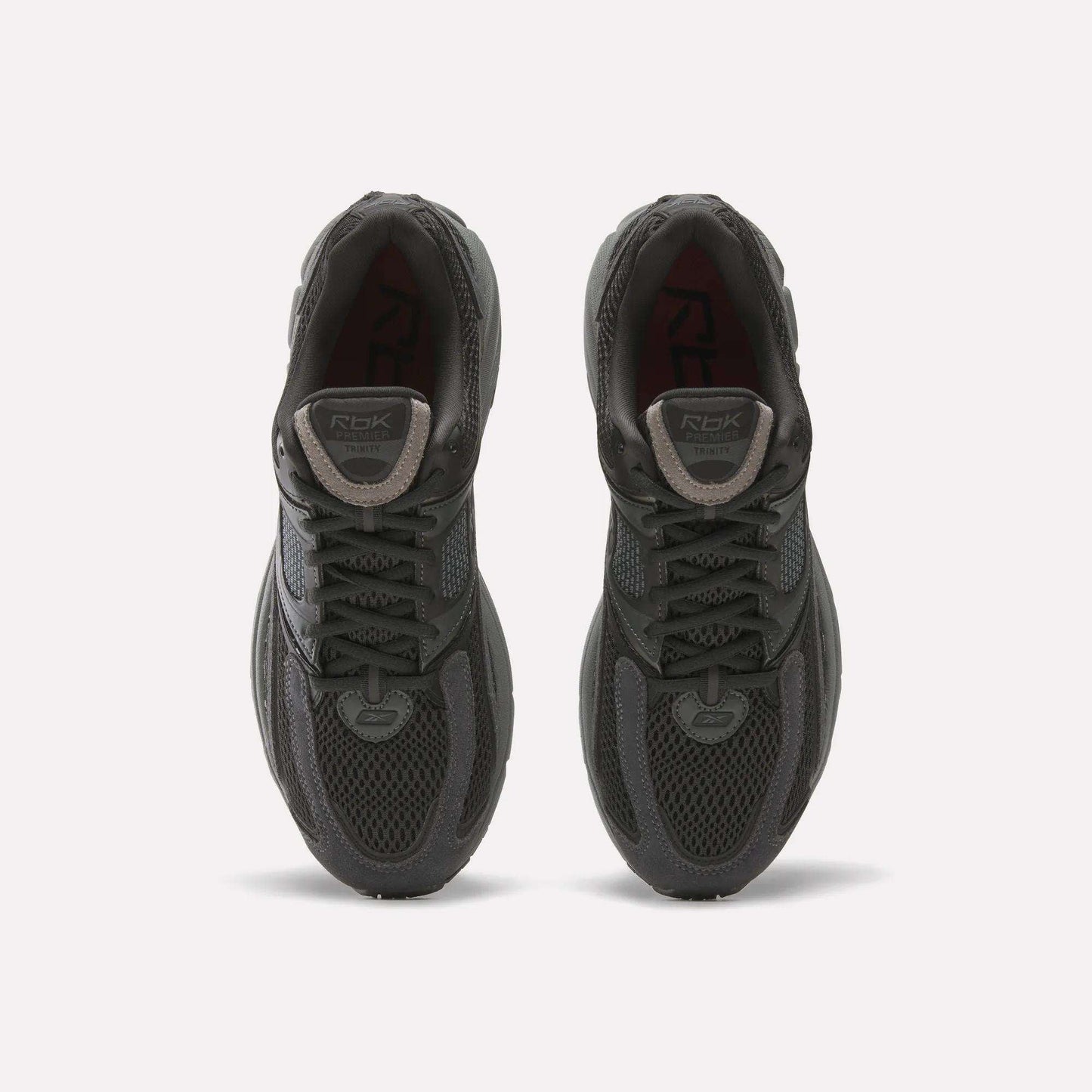 A pair of Reebok Premier Trinity women’s shoes in dark gray, viewed from above, with mesh uppers, laces, and logo patches on the tongues, side by side on a white background—ideal for running.