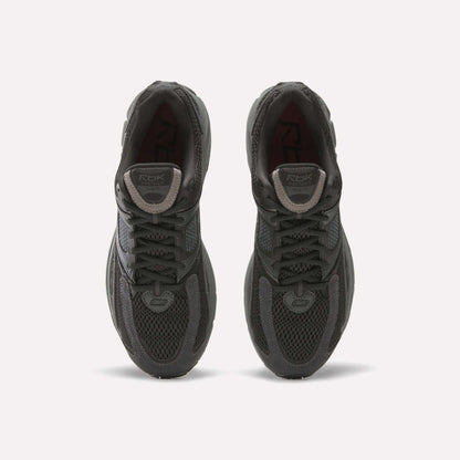A pair of Reebok Premier Trinity women’s shoes in dark gray, viewed from above, with mesh uppers, laces, and logo patches on the tongues, side by side on a white background—ideal for running.