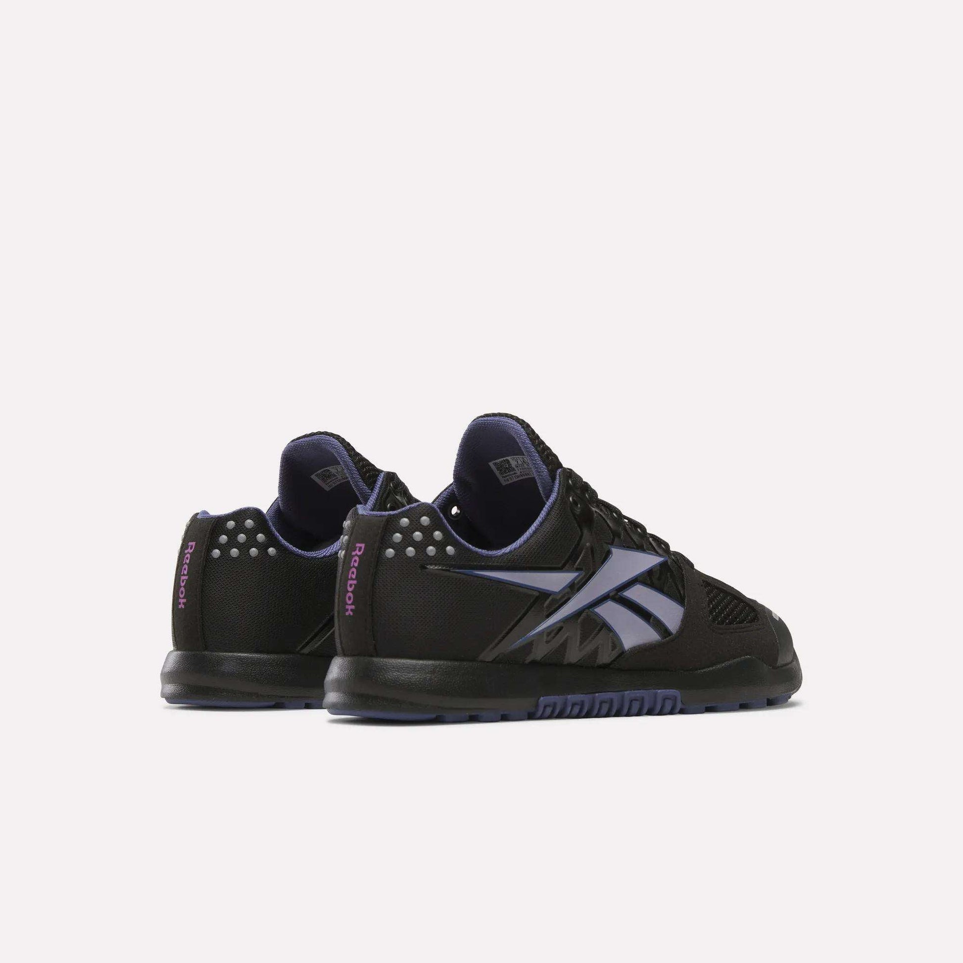 The Women's Nano 2.0 Training Shoes by Reebok are shown in black with purple accents, a large side Reebok logo, and decorative heel studs—ideal for functional fitness, displayed from a rear side angle on a white background.