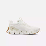 The Women's Zig Dynamica STR Shoes by Reebok feature a white design with a chunky, wavy FuelFoam midsole and tan accents, shown in side profile against a plain white background.