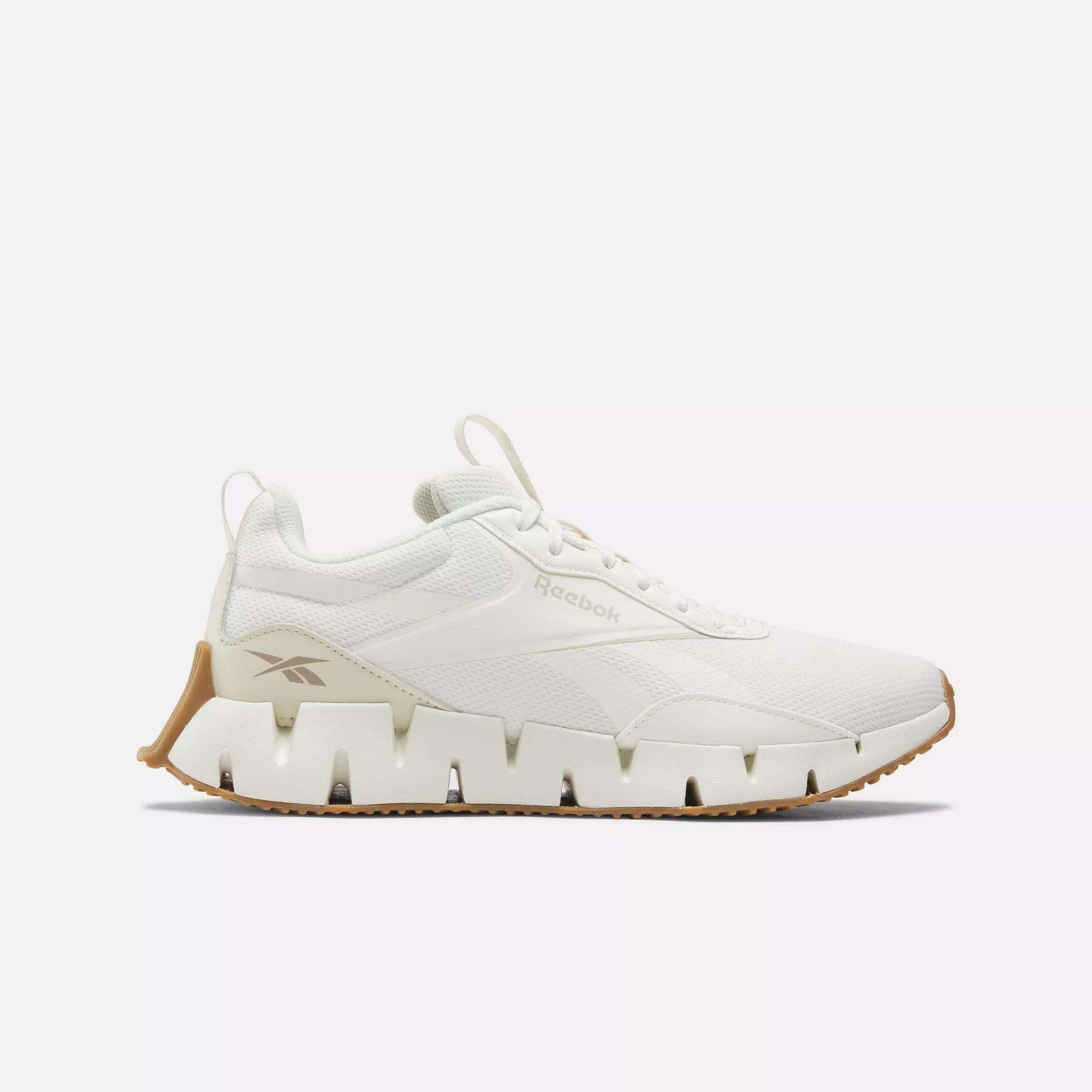 The Women's Zig Dynamica STR Shoes by Reebok feature a white design with a chunky, wavy FuelFoam midsole and tan accents, shown in side profile against a plain white background.