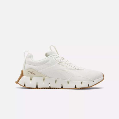 The Women's Zig Dynamica STR Shoes by Reebok feature a white design with a chunky, wavy FuelFoam midsole and tan accents, shown in side profile against a plain white background.