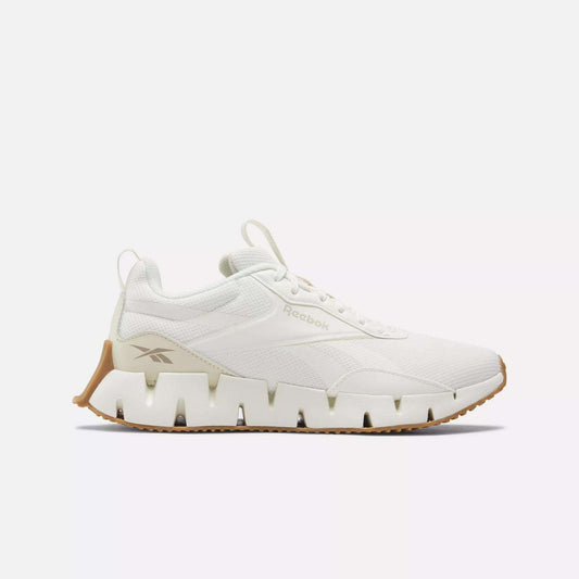 The Women's Zig Dynamica STR Shoes by Reebok feature a white design with a chunky, wavy FuelFoam midsole and tan accents, shown in side profile against a plain white background.