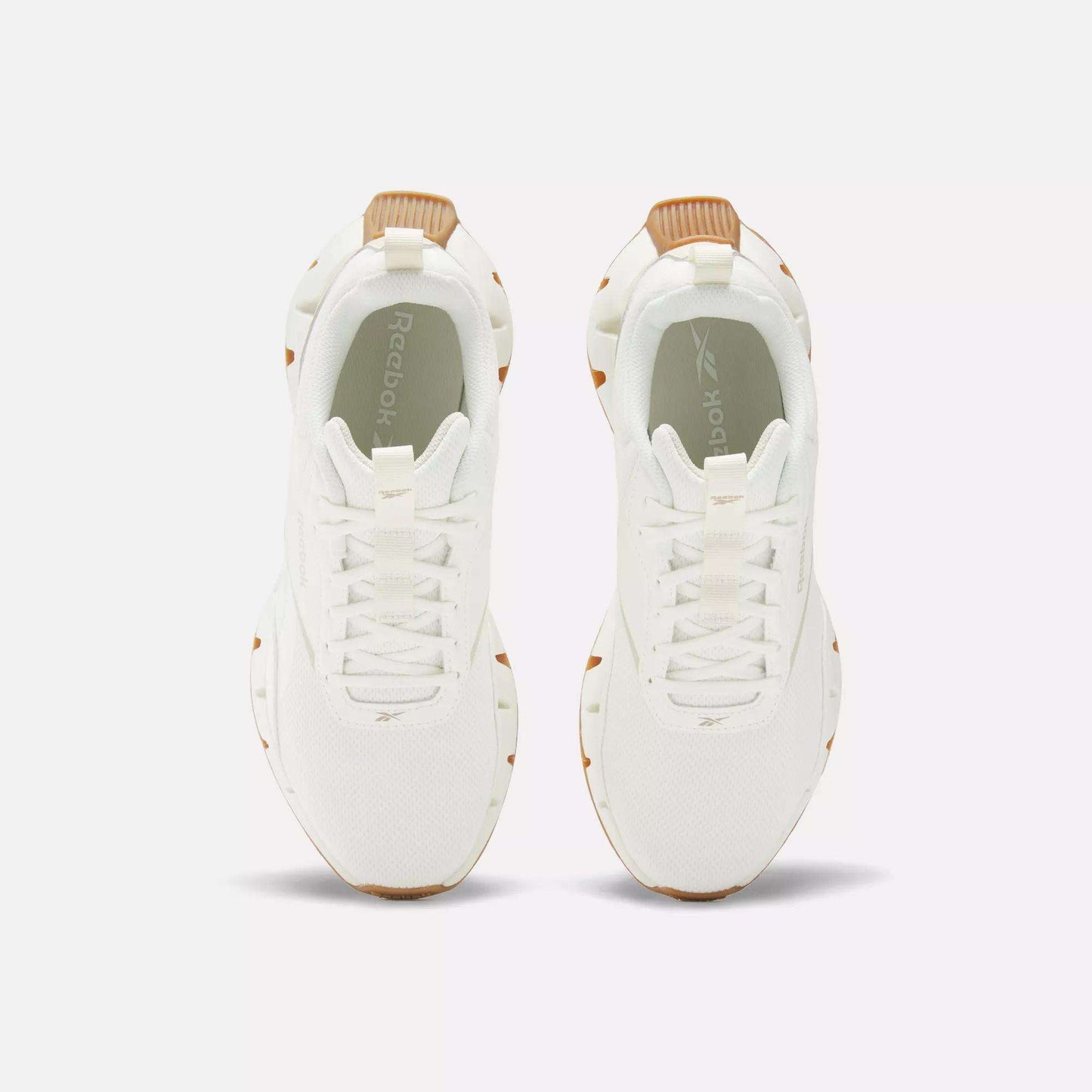 Top view of Reebok Women's Zig Dynamica STR Shoes, featuring white sneakers with tan accents on the heel and sole, displayed side by side on a plain white background.