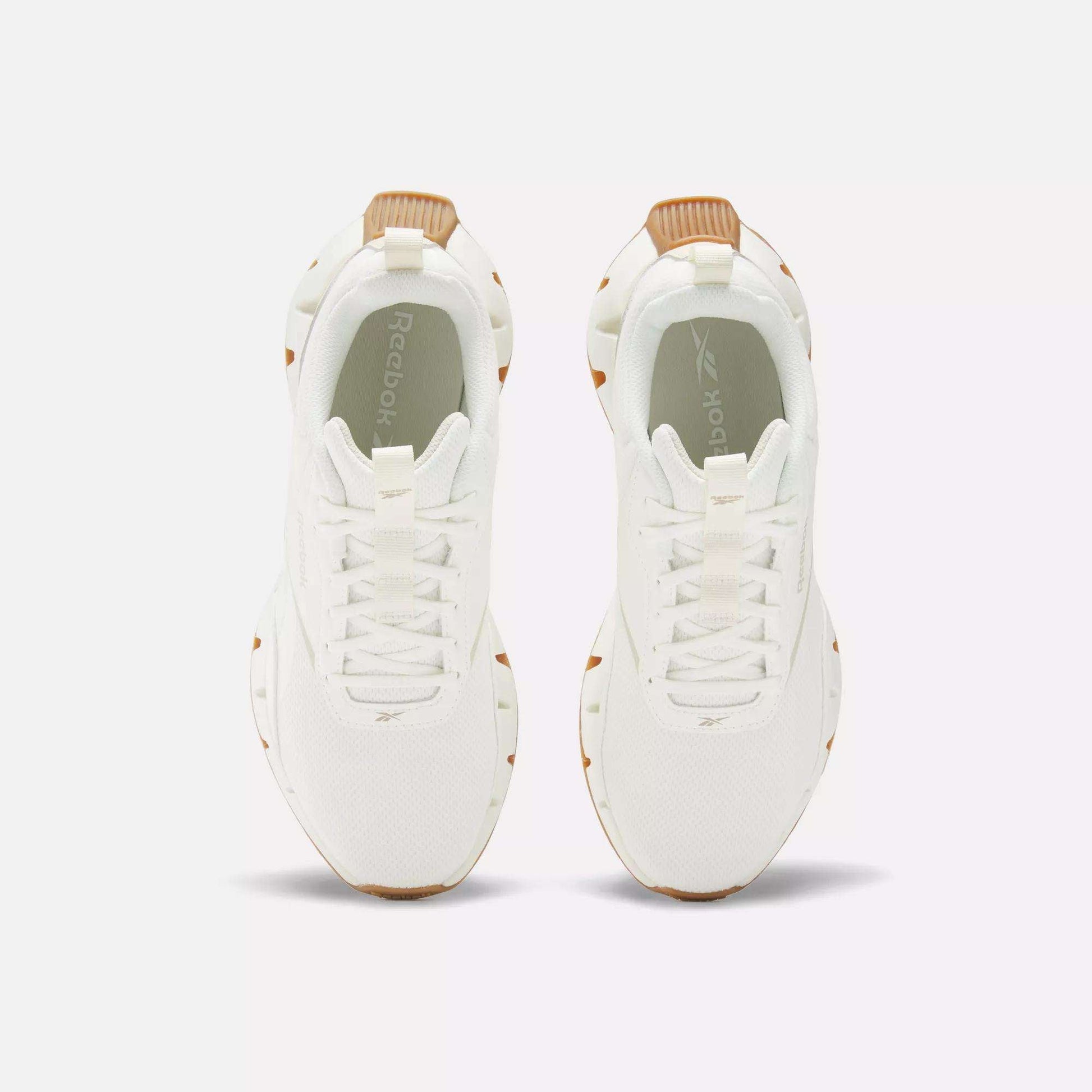 Top view of Reebok Women's Zig Dynamica STR Shoes, featuring white sneakers with tan accents on the heel and sole, displayed side by side on a plain white background.