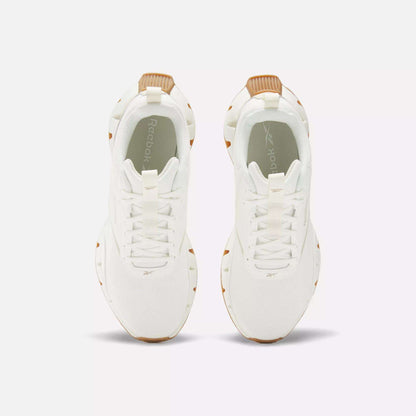 Top view of Reebok Women's Zig Dynamica STR Shoes, featuring white sneakers with tan accents on the heel and sole, displayed side by side on a plain white background.