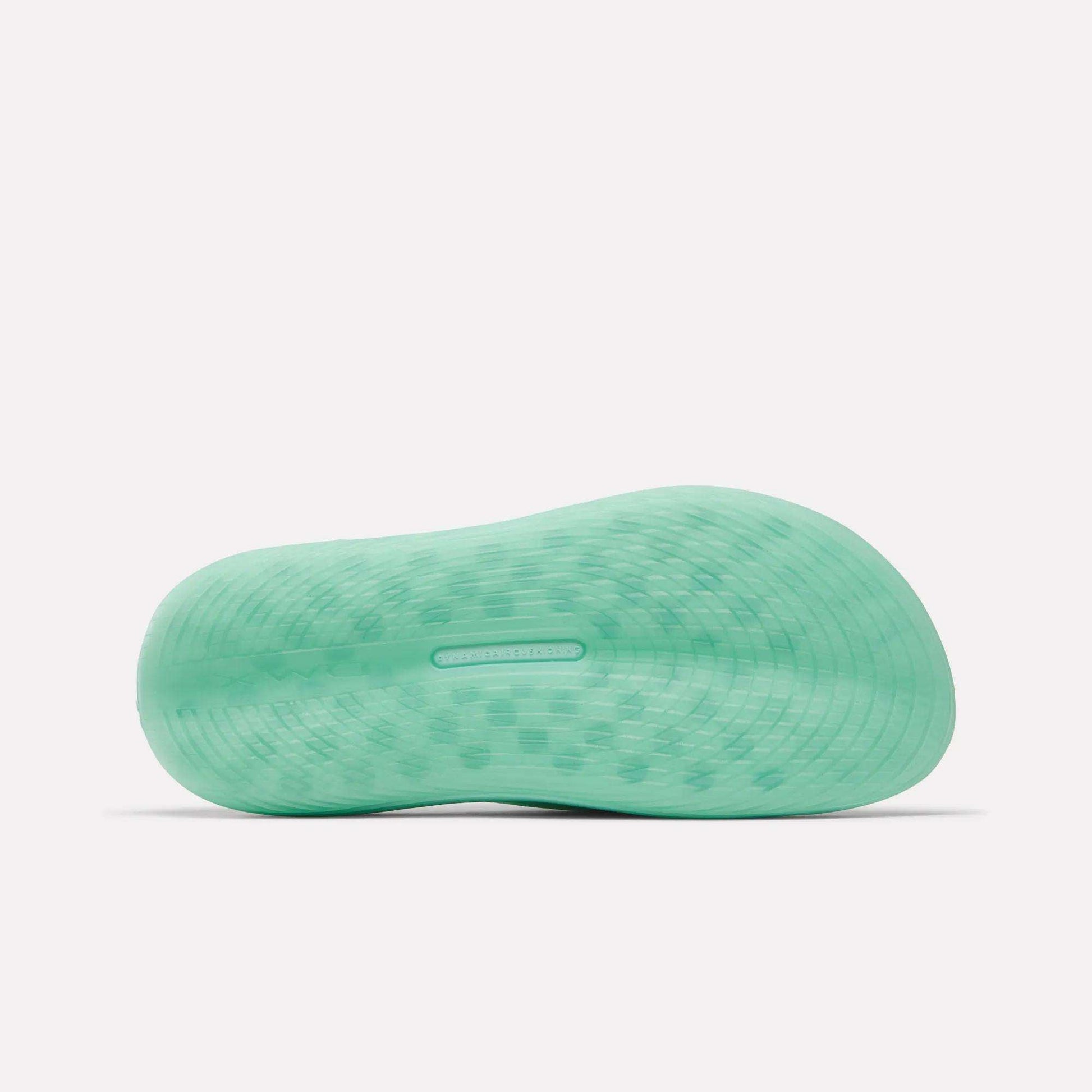 The image displays the light green textured sole of the Reebok DMX Recovery Walking Slides, shown from below on a white background. The wavy tread offers traction and comfort with moving air cushioning technology.