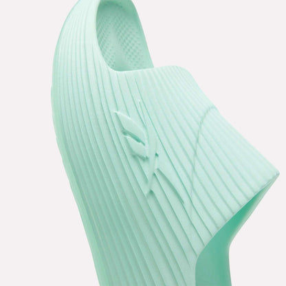 Close-up of a light mint green Reebok DMX Recovery Walking Slide, showing its ribbed texture, raised side logo, and airy foam-like cushioning for comfort.