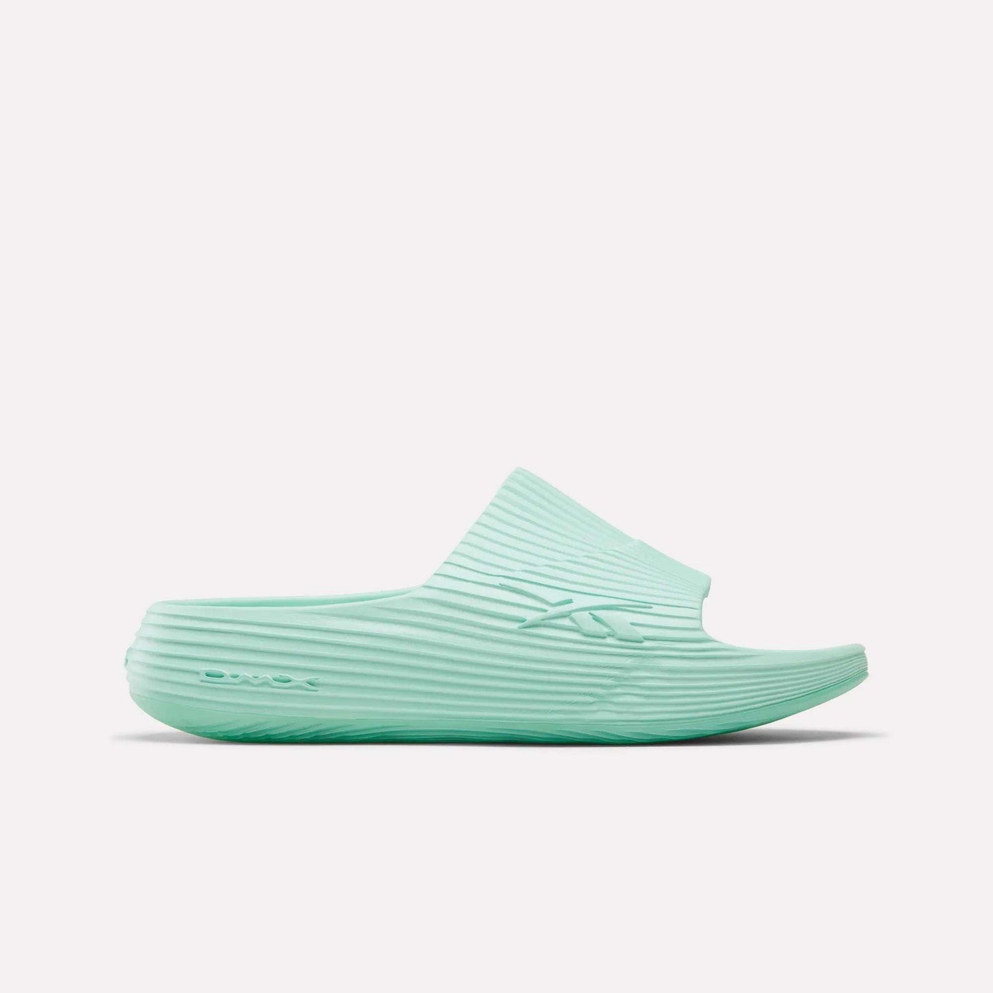 The Reebok DMX Recovery Walking Slides in light teal feature a ribbed texture, open toe, and thick sole with moving air cushioning, displayed in side profile on a white background.