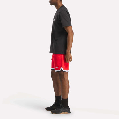 A person stands in profile wearing a black T-shirt, Reebok Men's Basketball Transition Shorts 7" in red with white trim, black socks, and black sneakers against a plain white background.