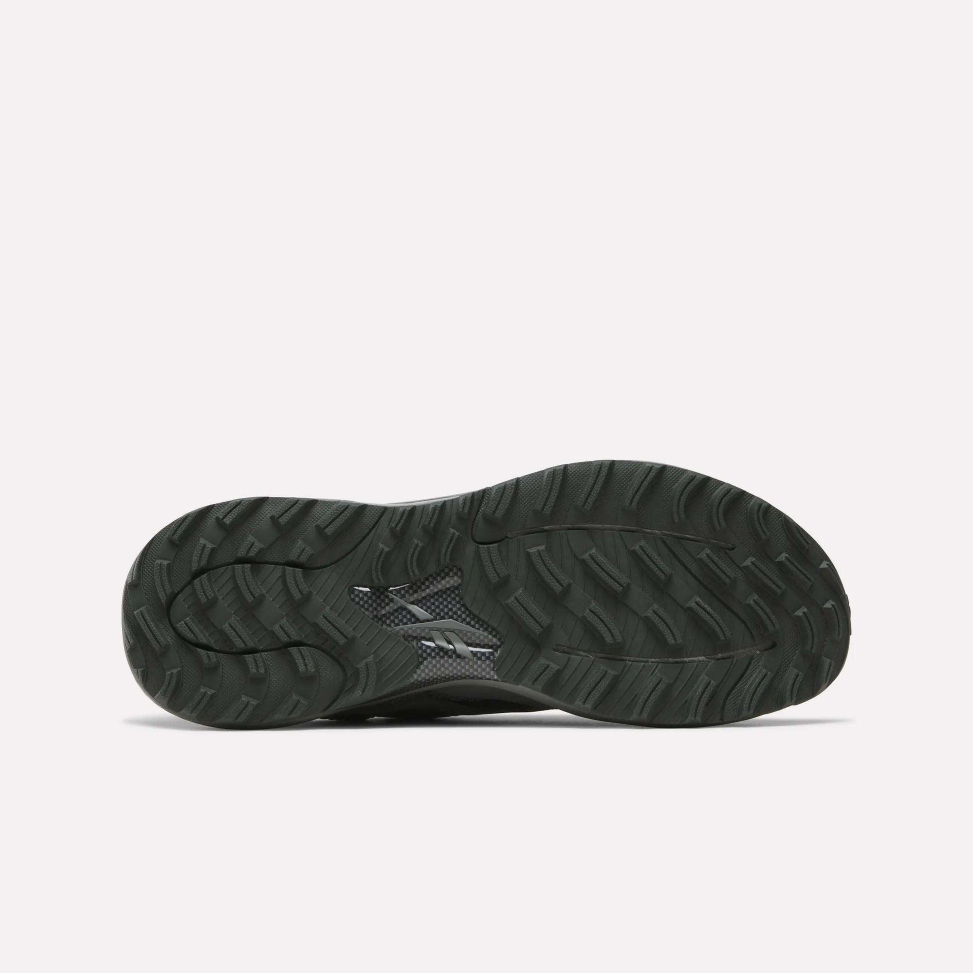 The image shows the black, textured rubber outsole of Reebok's Nano Golf Shoes with a wavy tread pattern and small logo near the center, designed to complement its lightweight FlexWeave upper. The background is plain white.