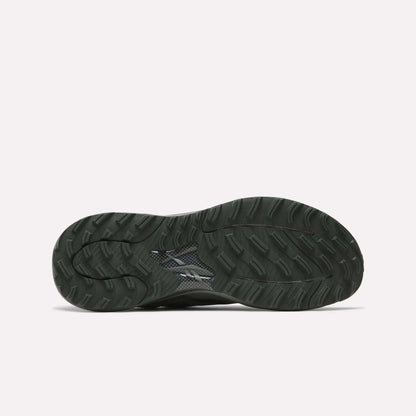 The image shows the black, textured rubber outsole of Reebok's Nano Golf Shoes with a wavy tread pattern and small logo near the center, designed to complement its lightweight FlexWeave upper. The background is plain white.