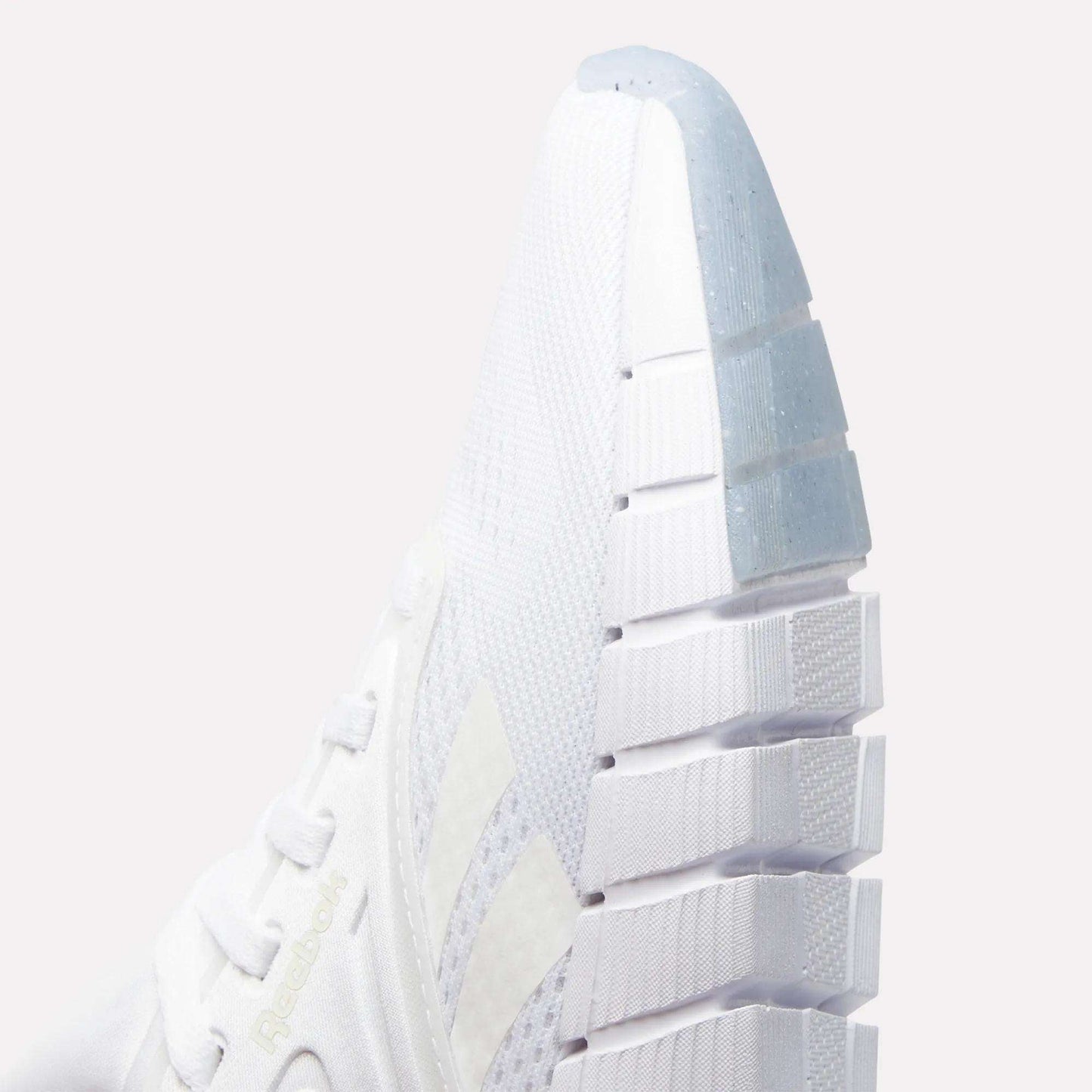 Close-up of the front and side of a white Reebok Women's Nano Gym Training Shoe featuring textured mesh fabric, white laces, a thick grooved sole, and the Reebok logo subtly displayed on the side.