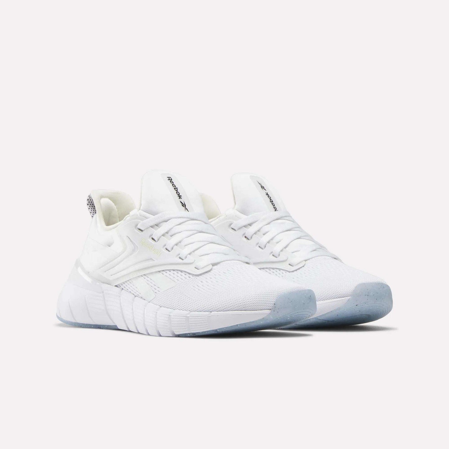 A pair of Women's Nano Gym Training Shoes by Reebok featuring white mesh uppers, light blue translucent soles, and Reebok logos on the tongue and side, displayed against a plain light background.