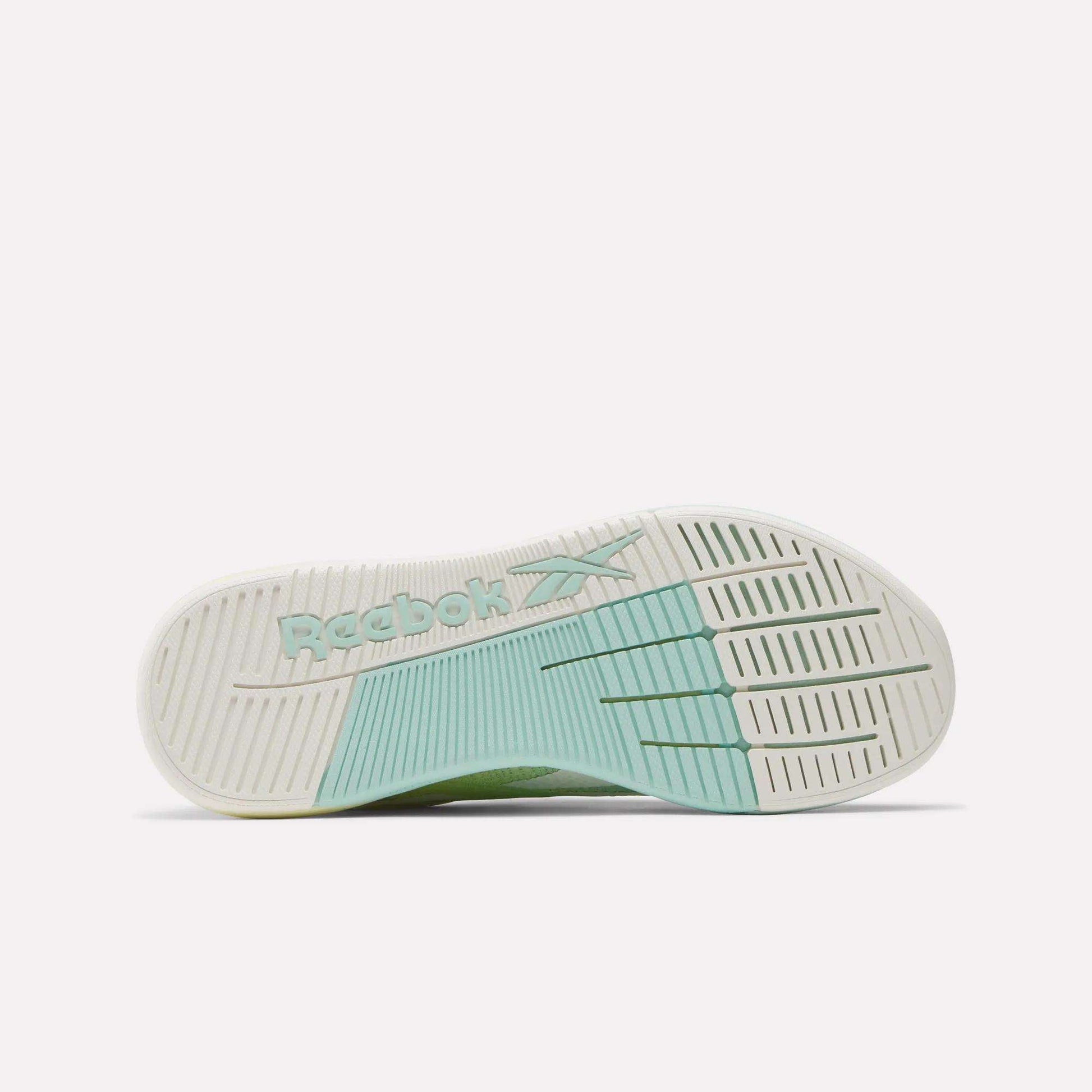 The image displays the sole of Reebok Women's Nano X5 Training Shoes, featuring a white and light green tread. The embossed green Reebok logo at the center adds a stylish touch, making these sneakers appealing for women.