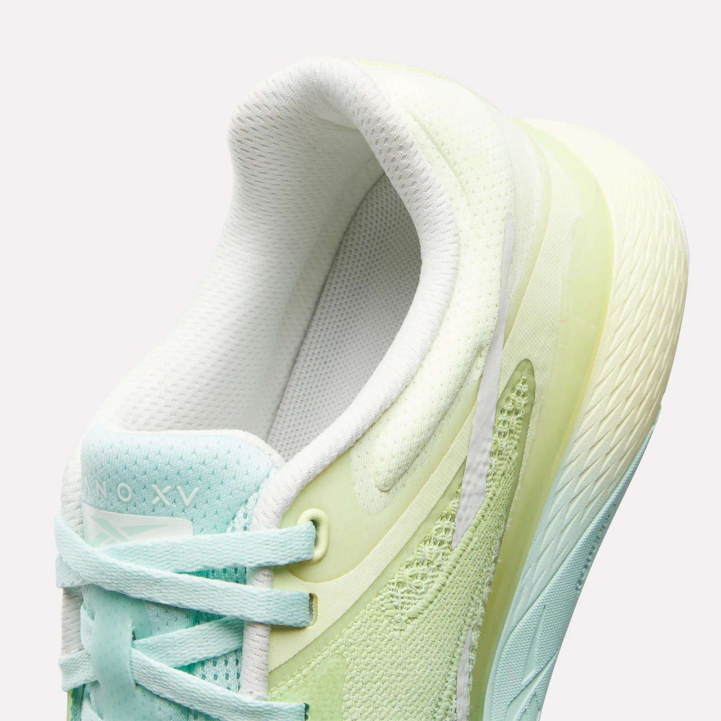 A close-up of the Reebok Women's Nano X5 Training Shoes shows pastel light green and aqua hues, white laces, a textured sole, and a padded collar for comfort. The inner lining and tongue are white.