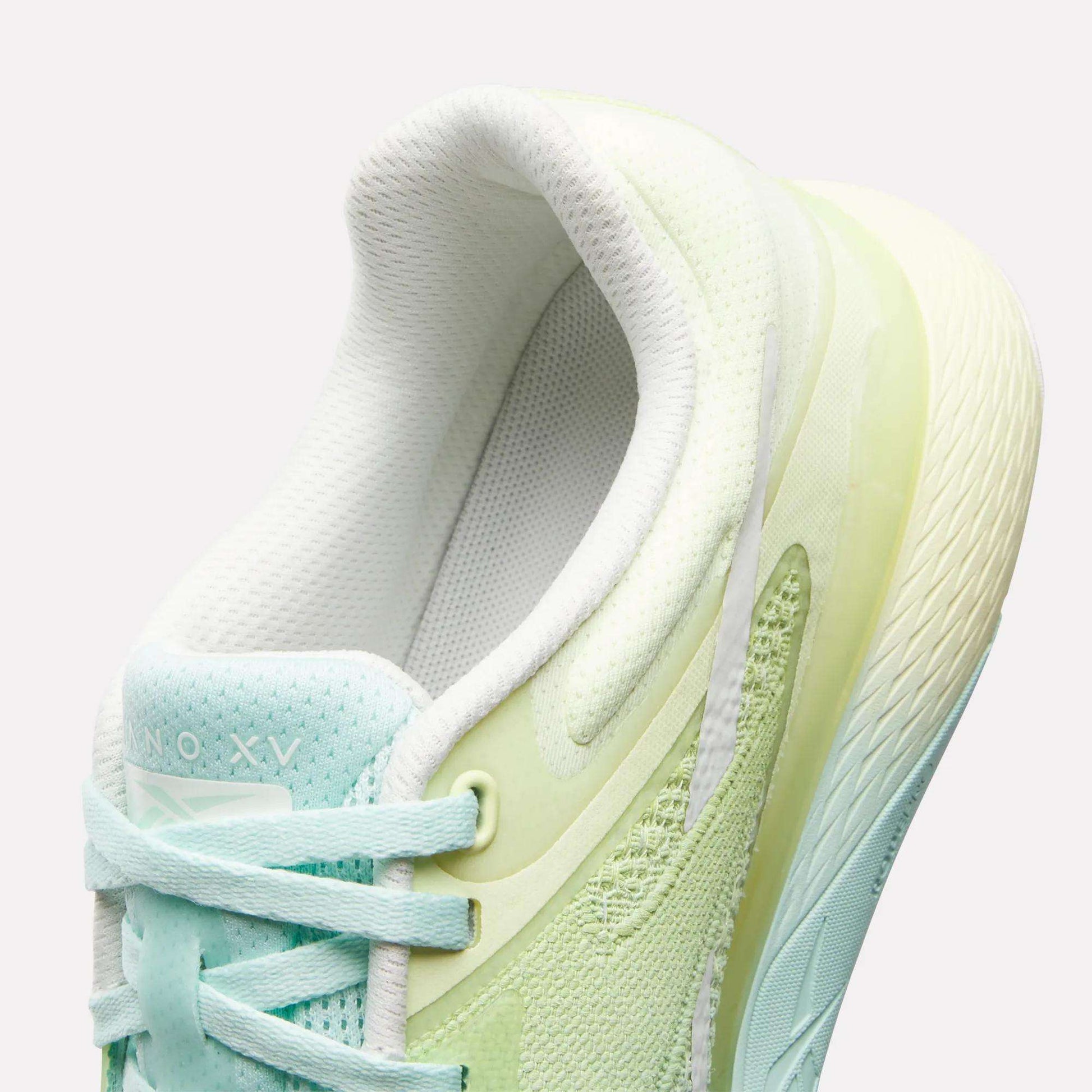 A close-up of the Reebok Women's Nano X5 Training Shoes shows pastel light green and aqua hues, white laces, a textured sole, and a padded collar for comfort. The inner lining and tongue are white.