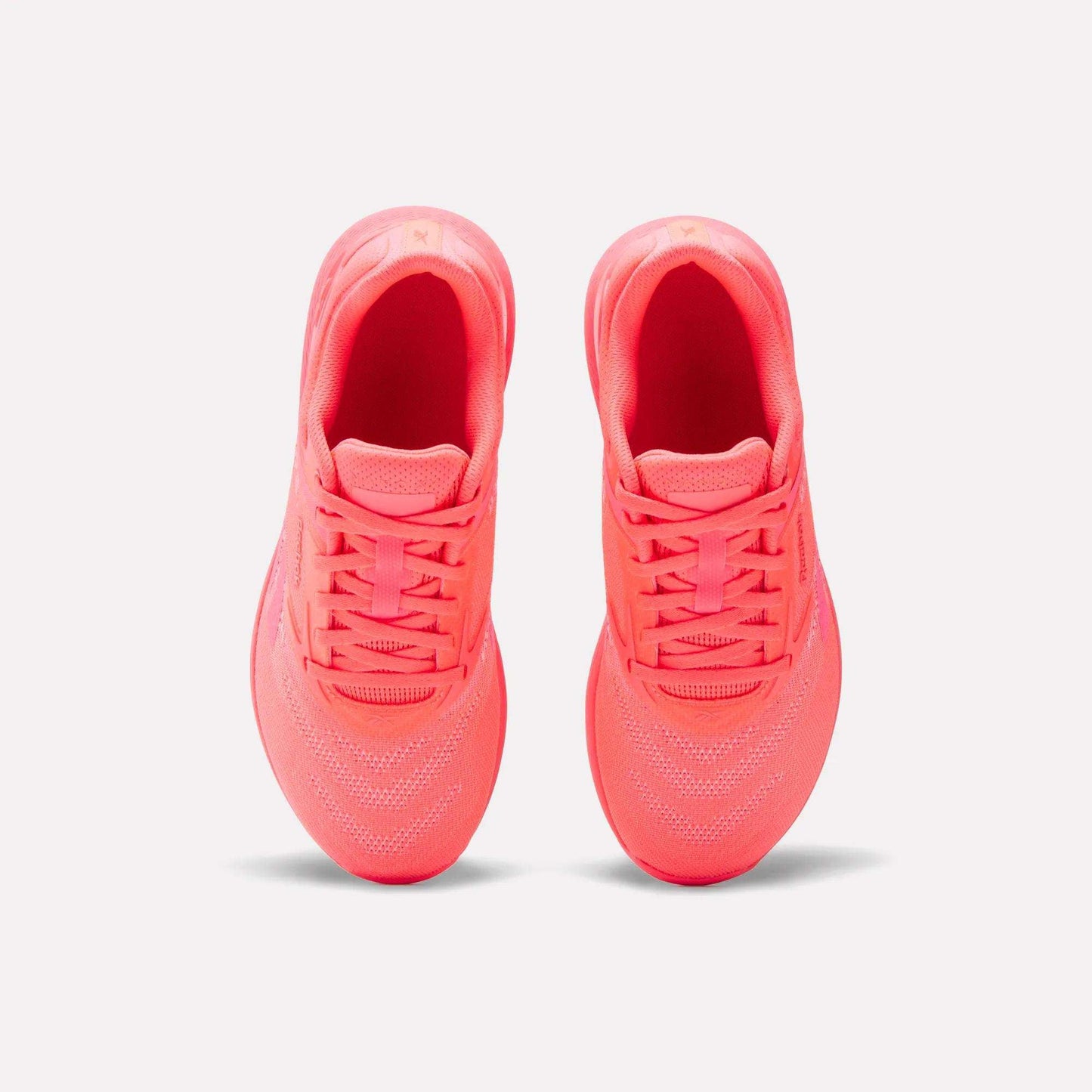 A pair of Reebok Women's Nano X5 Training Shoes in neon pink is shown from above, highlighting the tops, laces, and mesh details against a plain white background.