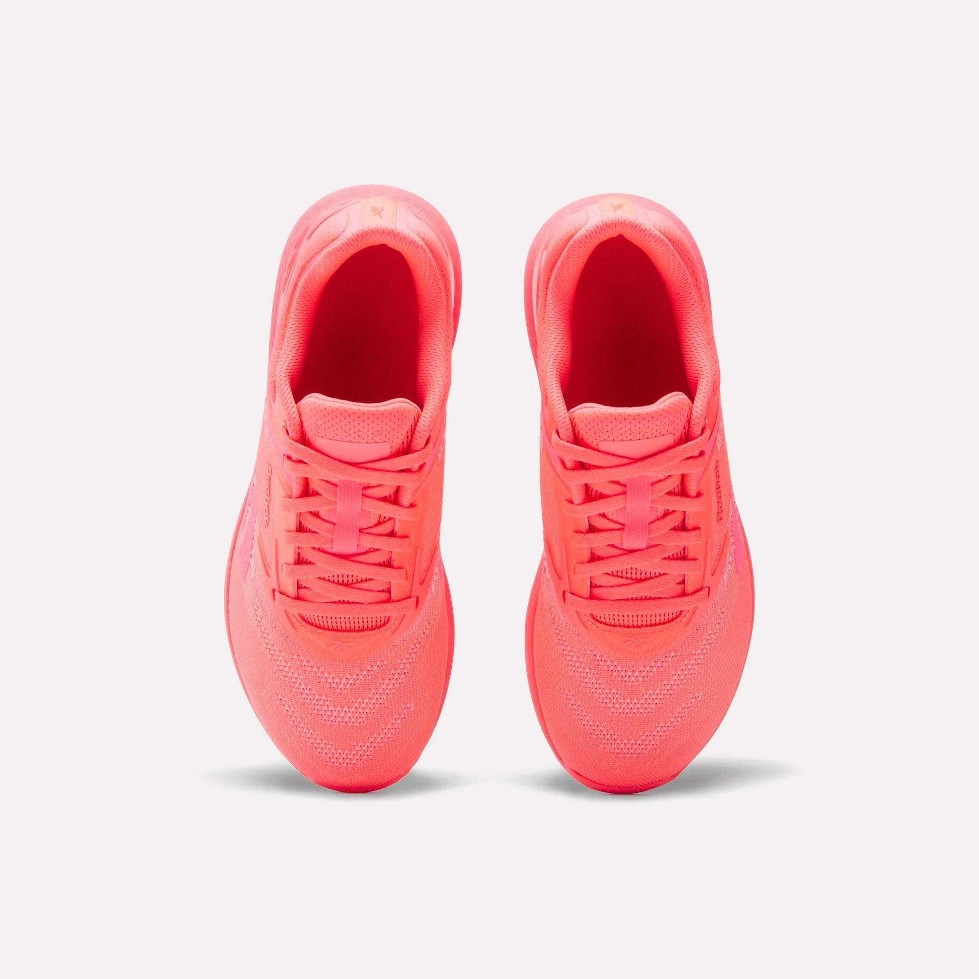 A pair of Reebok Women's Nano X5 Training Shoes in neon pink is shown from above, highlighting the tops, laces, and mesh details against a plain white background.