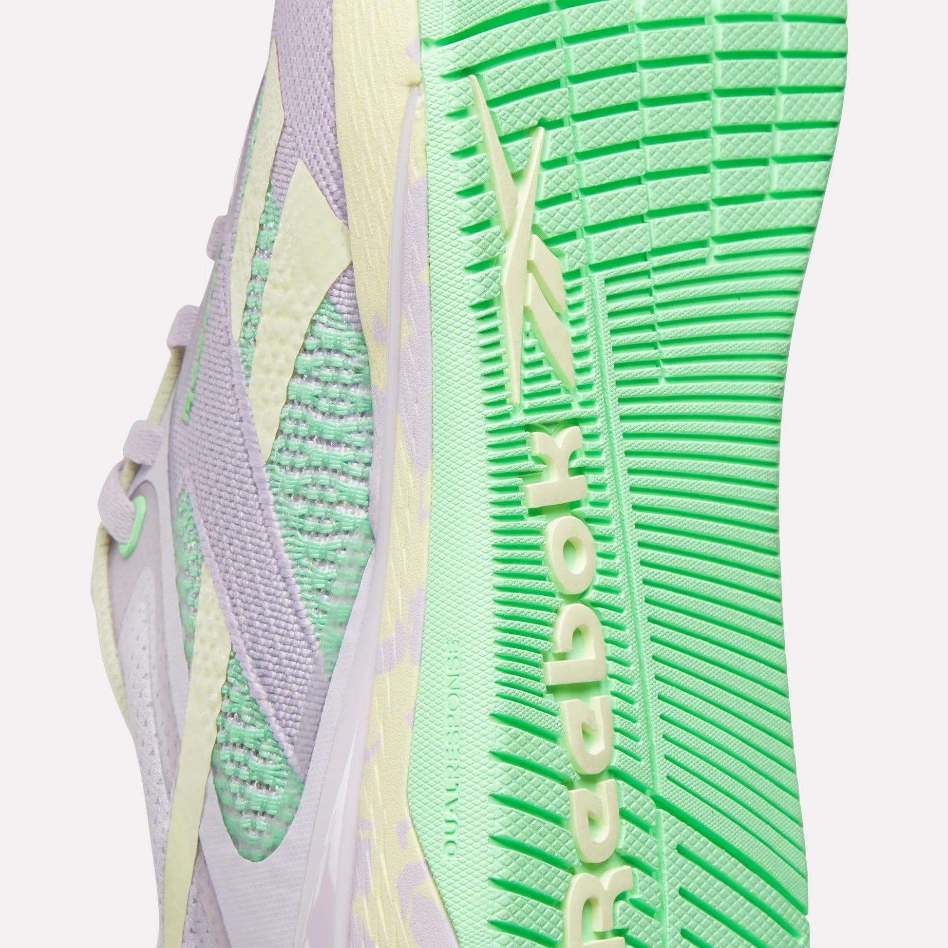 Close-up of Reebok Women's Nano X5 Training Shoes, iconic for training, with a light purple and mint green knit upper, textured mint green sole, and the Reebok logo in light yellow on the side and sole.