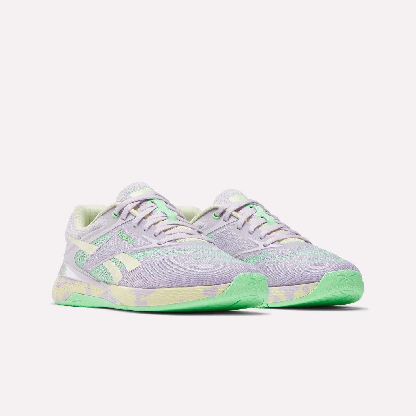 The Reebok Women's Nano X5 Training Shoes are pastel purple with light green accents and soles, plus white side stripes and a green-and-yellow midsole pattern. Comfortable running shoes displayed on a plain white background.