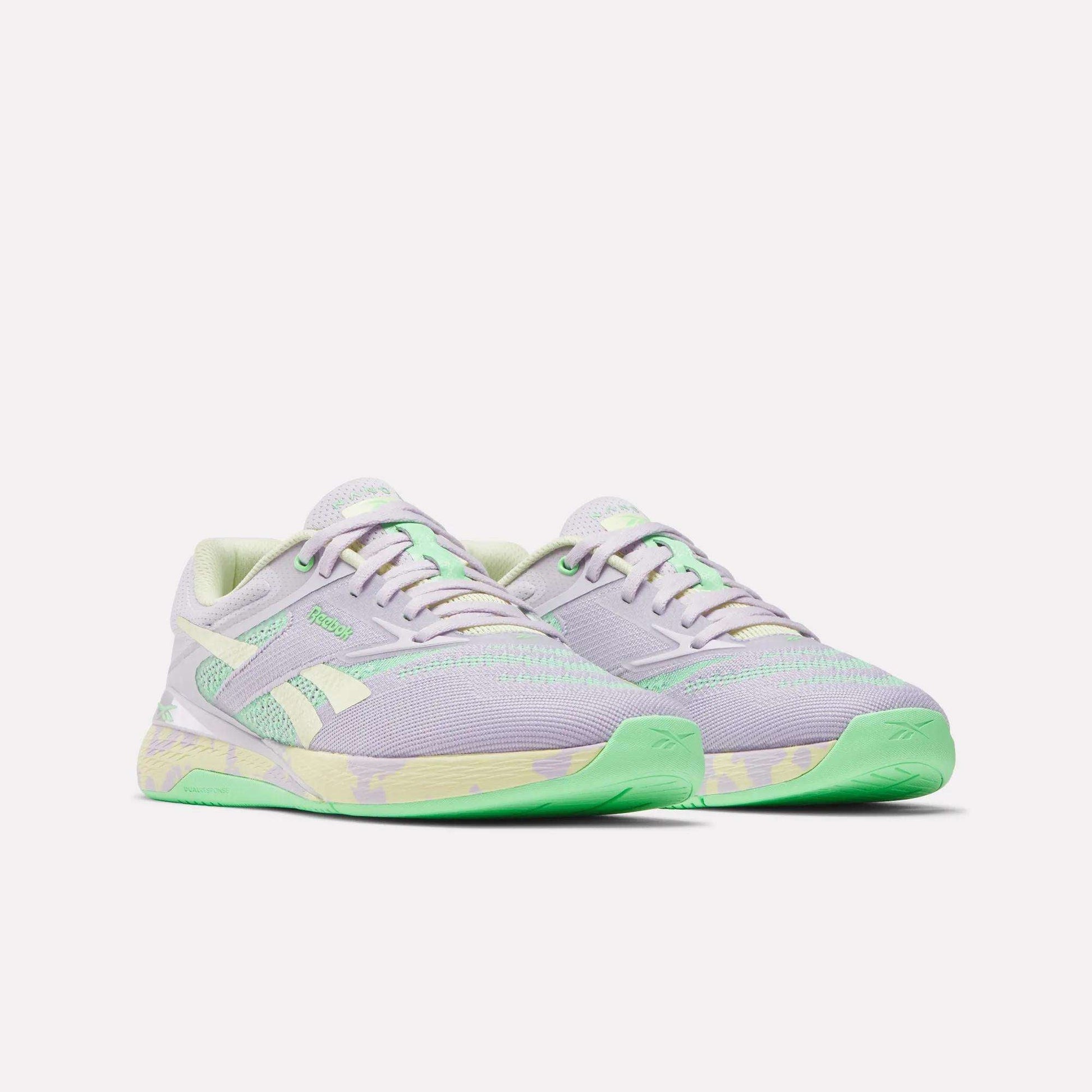 The Reebok Women's Nano X5 Training Shoes are pastel purple with light green accents and soles, plus white side stripes and a green-and-yellow midsole pattern. Comfortable running shoes displayed on a plain white background.