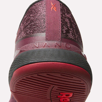 Close-up of the heel and sole of Reebok Women's Nano X5 Training Shoes in burgundy, featuring textured fabric, a red pull tab, "NANO" on the back, and a black and red rubber outsole for comfortable support.