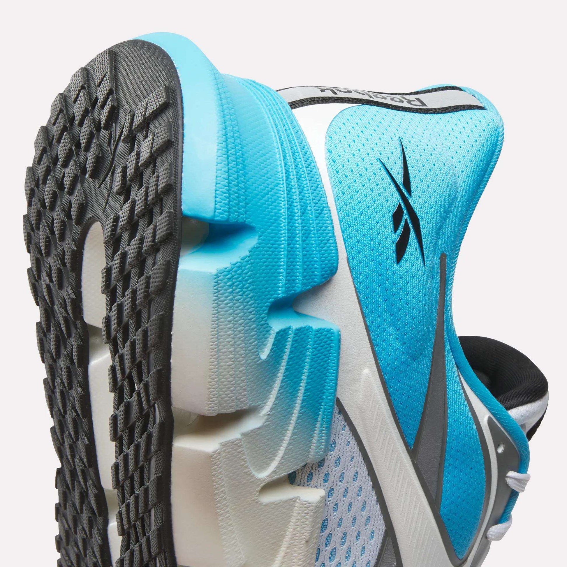Close-up of the Reebok Men's FloatZig 2 Running Shoes in blue, white, and black, featuring a mesh upper with logo detail and a textured sole. Superfloat+ cushioning delivers energy-returning comfort for sports activities.