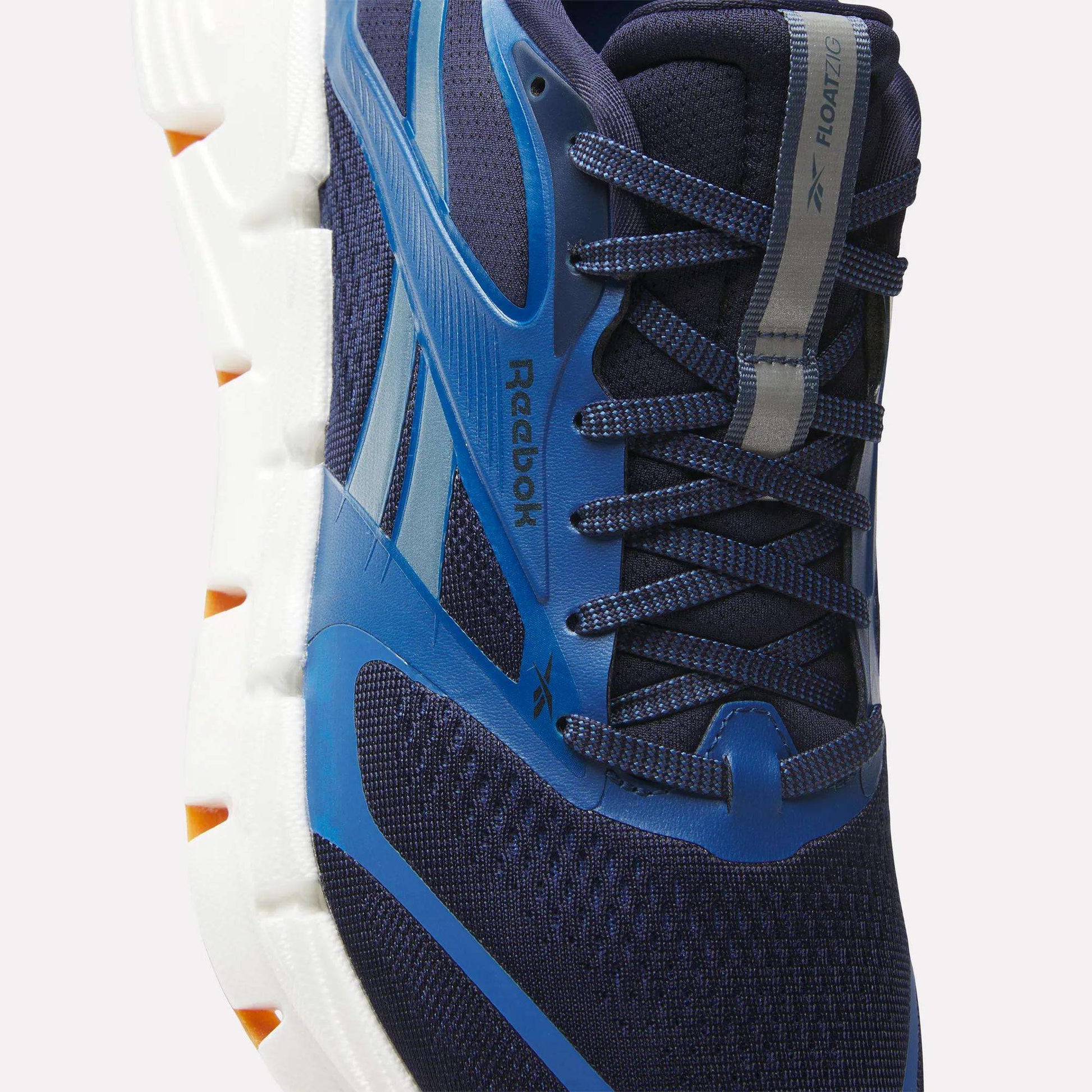 Close-up of Reebok Men's FloatZig 2 Running Shoes in navy and blue, featuring Superfloat+ cushioning, a white and orange sole, mesh upper, laces, and the Reebok logo on the side and tongue.