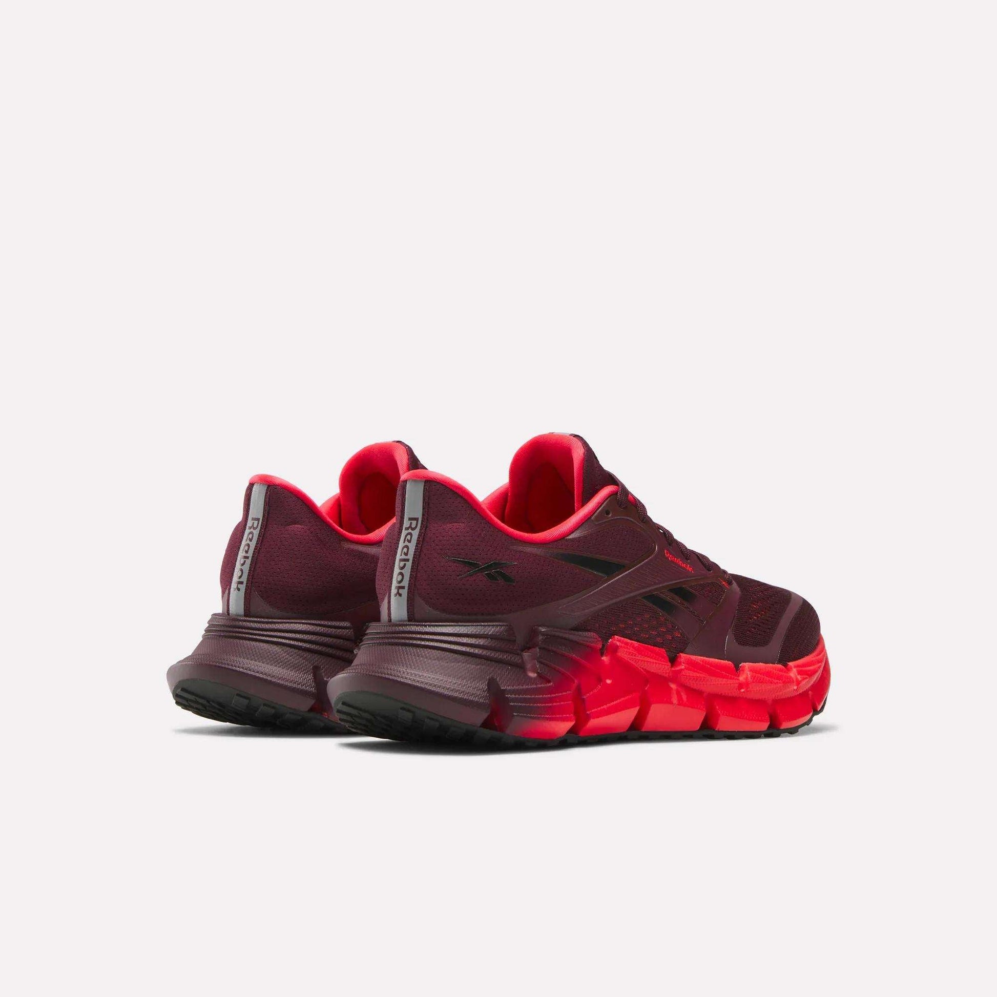 A pair of Reebok Women's FloatZig 2 Running Shoes in maroon and bright red is shown from the back and side, featuring chunky, textured soles with Superfloat+ cushioning and mesh uppers on a light background.