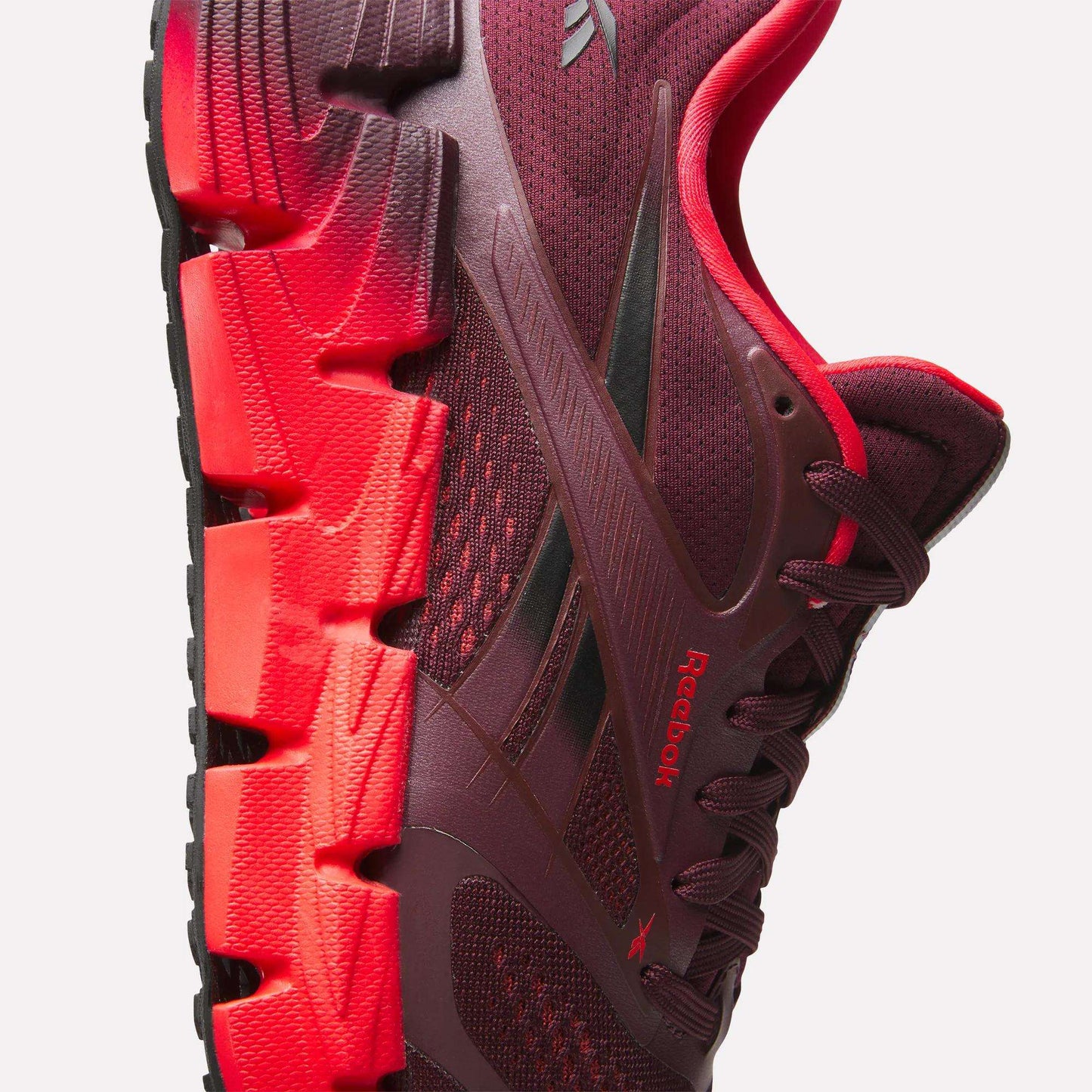 Side view of maroon and red Reebok Women's FloatZig 2 Running Shoes with Superfloat+ cushioning, chunky zigzag sole, and textured mesh upper. The Reebok logo appears on the side panel and tongue.