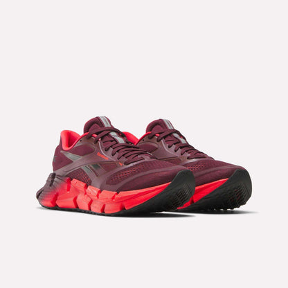 A pair of Reebok Women's FloatZig 2 Running Shoes in maroon with bright red midsoles, black outsoles, mesh uppers, and Superfloat+ cushioning are displayed on a plain white background.