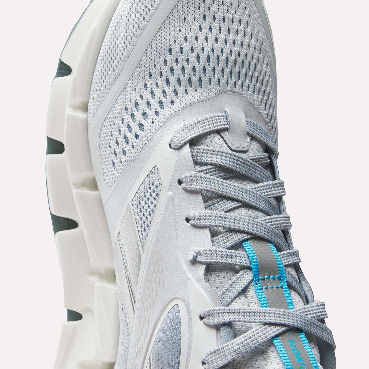 Close-up of Reebok Women's FloatZig 2 Running Shoes in light gray with mesh fabric, gray laces, blue tongue accents, Superfloat+ cushioning for comfort, and a durable white sole with deep grooves.