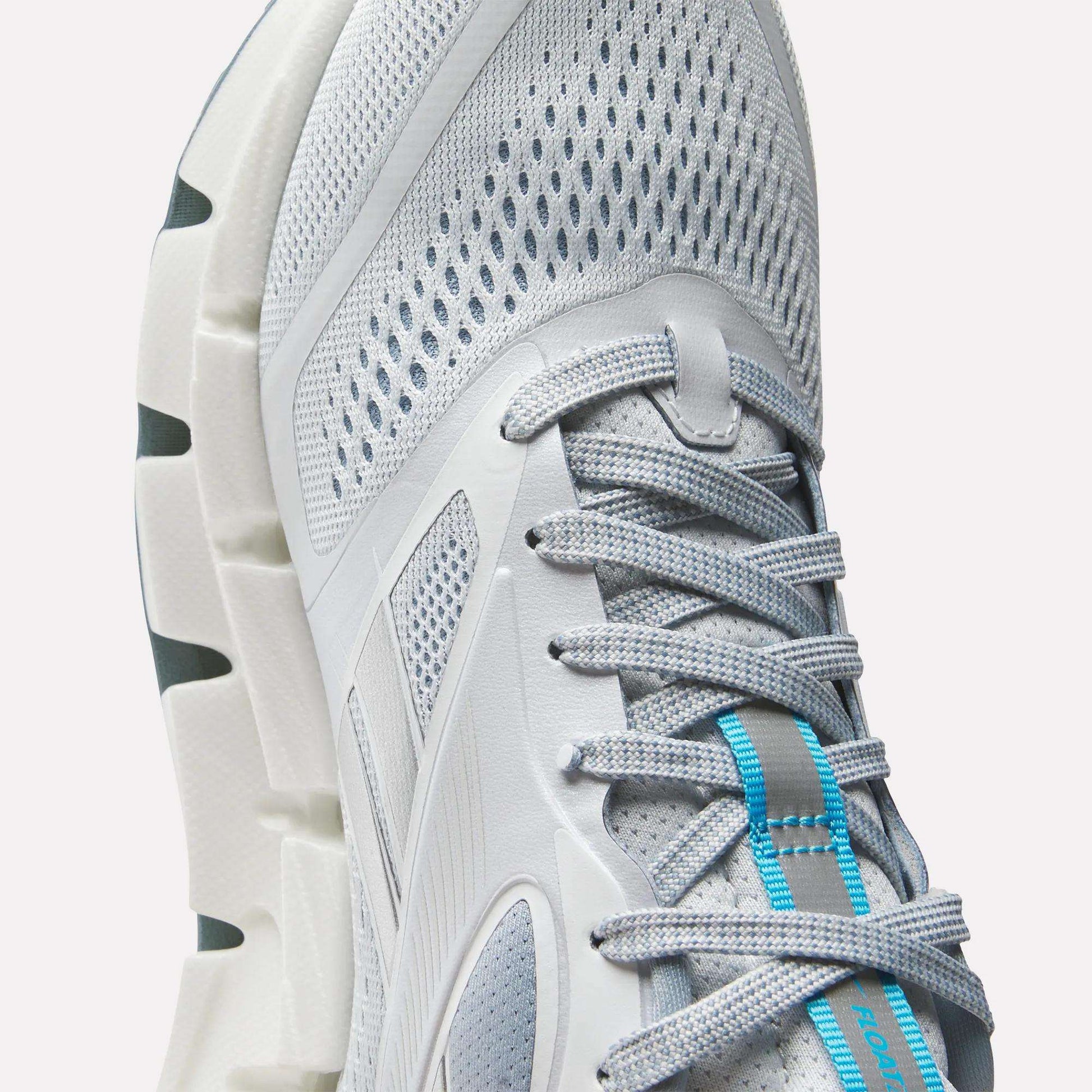 Close-up of Reebok Women's FloatZig 2 Running Shoes in light gray with mesh fabric, gray laces, blue tongue accents, Superfloat+ cushioning for comfort, and a durable white sole with deep grooves.