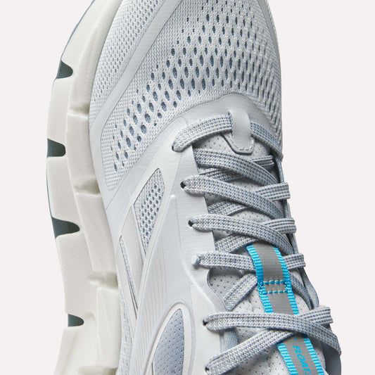 Close-up of Reebok Women's FloatZig 2 Running Shoes in light gray with mesh fabric, gray laces, blue tongue accents, Superfloat+ cushioning for comfort, and a durable white sole with deep grooves.