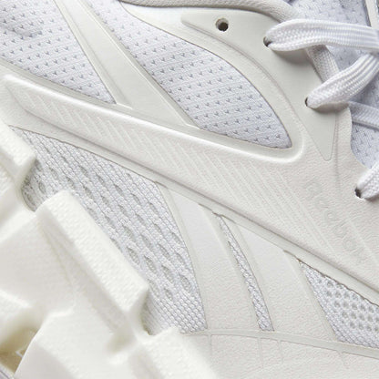 Close-up of Reebok Women's FloatZig 2 Running Shoes in white, showcasing textured mesh, synthetic overlays, intricate stitching, subtle branding, and a chunky sculpted sole with Superfloat+ cushioning.