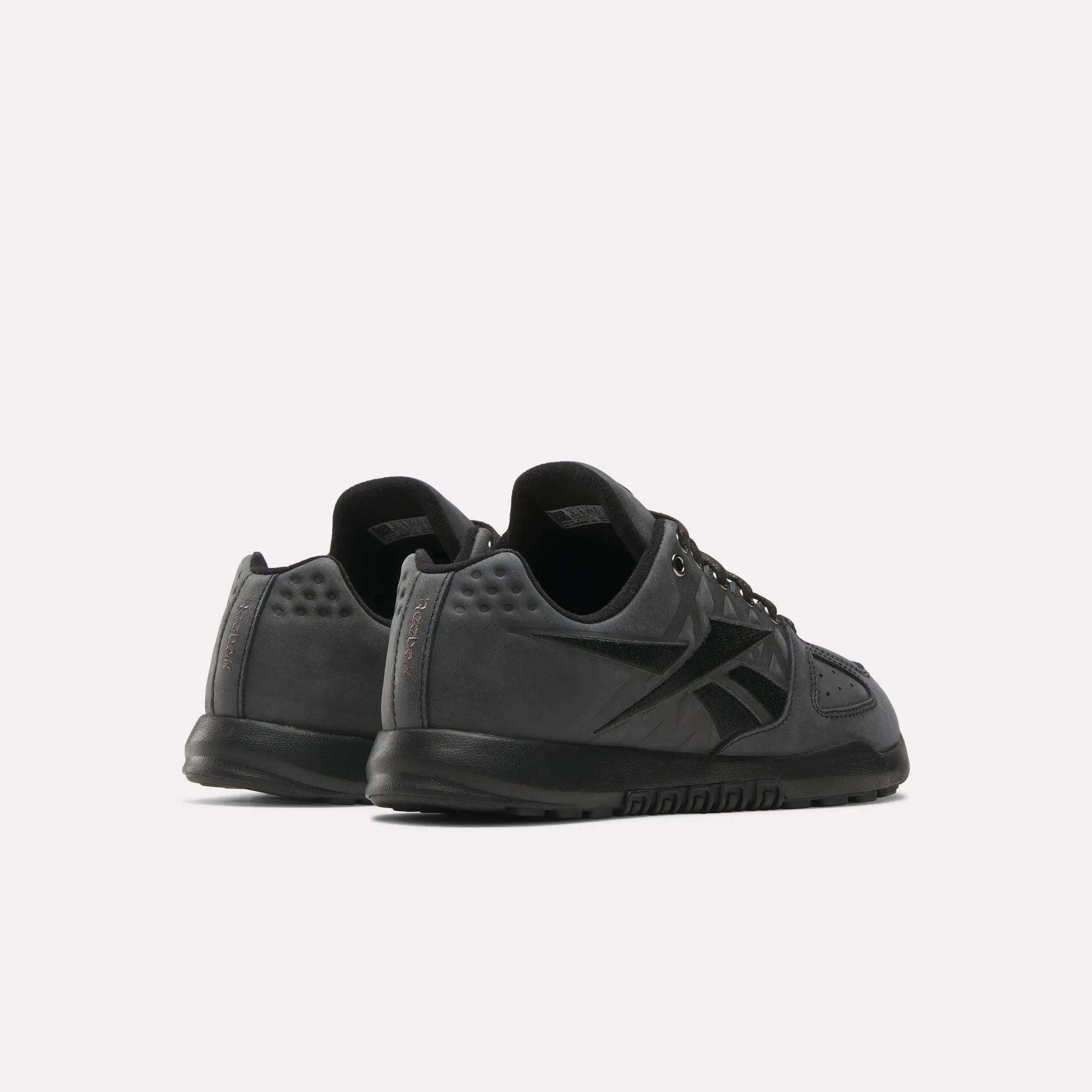 The Reebok Nano 2.0 Training Shoes, shown in black with a low-top design and pebbled leather detail, are displayed from back and side views against a plain white background.