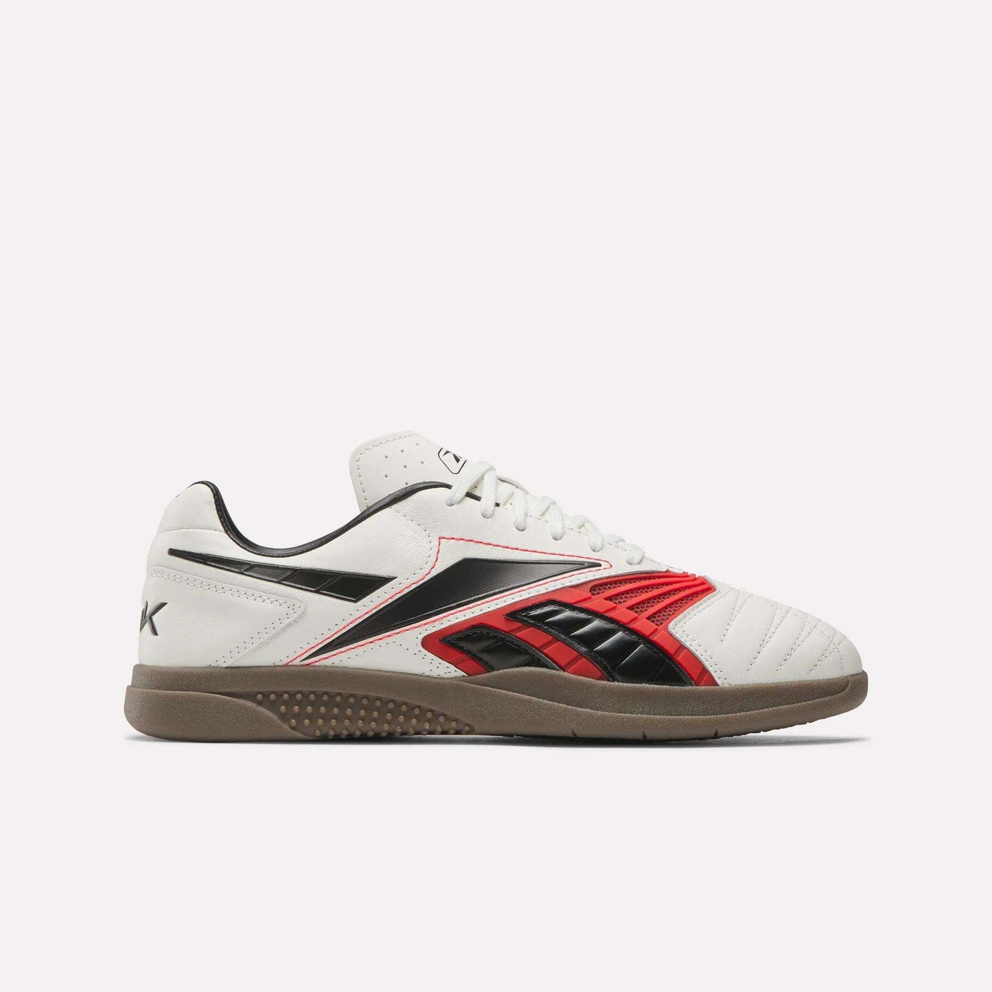 The Reebok Hammer Valde Shoes are white indoor soccer boots with red and black accents, a lace-up leather upper, low profile gum rubber sole, visible stitching, and classic Reebok branding on the side and heel.