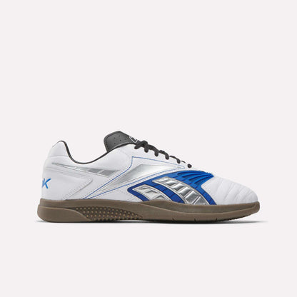 The Reebok Hammer Valde Shoes are white indoor soccer boots with a leather upper, blue, silver, and black accents, gum rubber sole, and black laces shown in side profile on a plain white background.