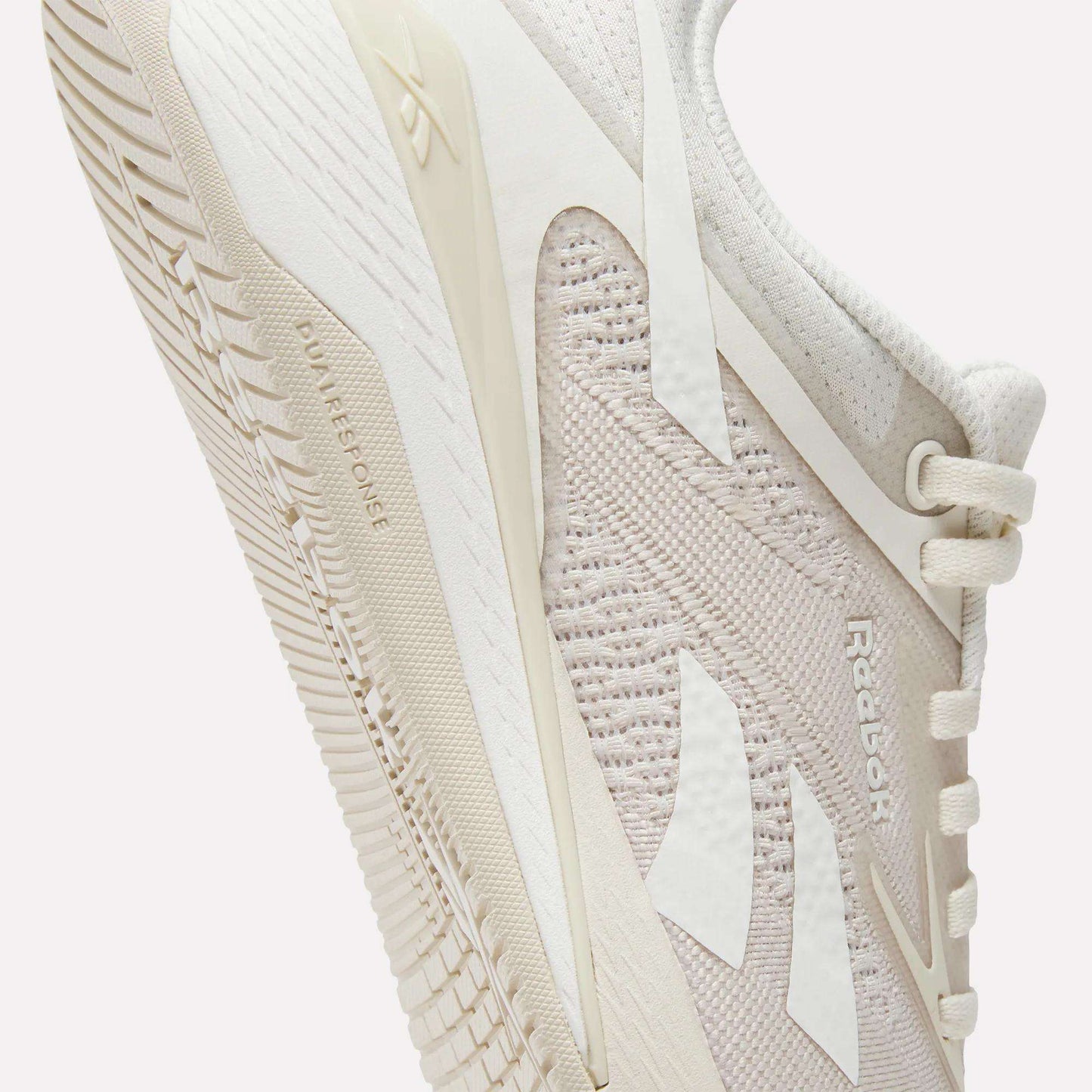 A close-up of Reebok Women's Nano X5 Training Shoes in light beige, highlighting the side mesh texture, Reebok logo, and detailed sole featuring the "DUAL DENSITY" text.