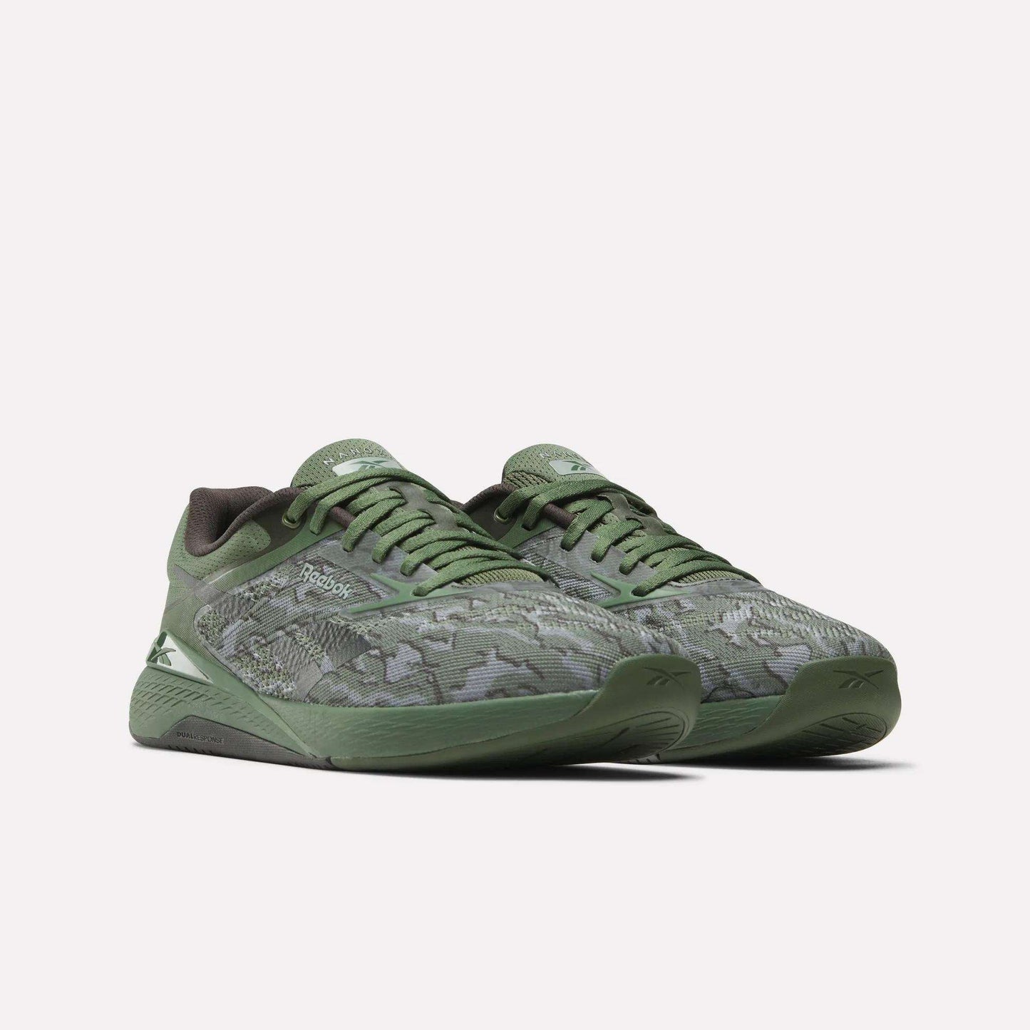 The Reebok Nano X5 Training Shoes for men feature a green camouflage pattern, dark green soles, and Reebok logos on the side and tongue. These iconic shoes are displayed against a plain white background.